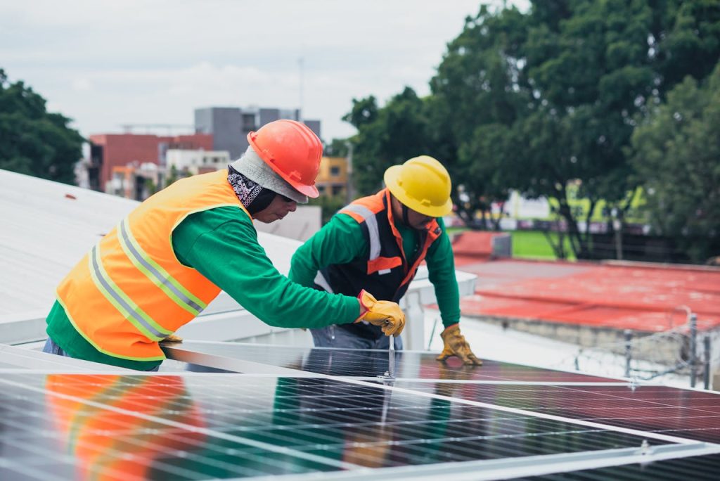 Two workers installing rooftop solar panels safely equipped with PPE and tools.